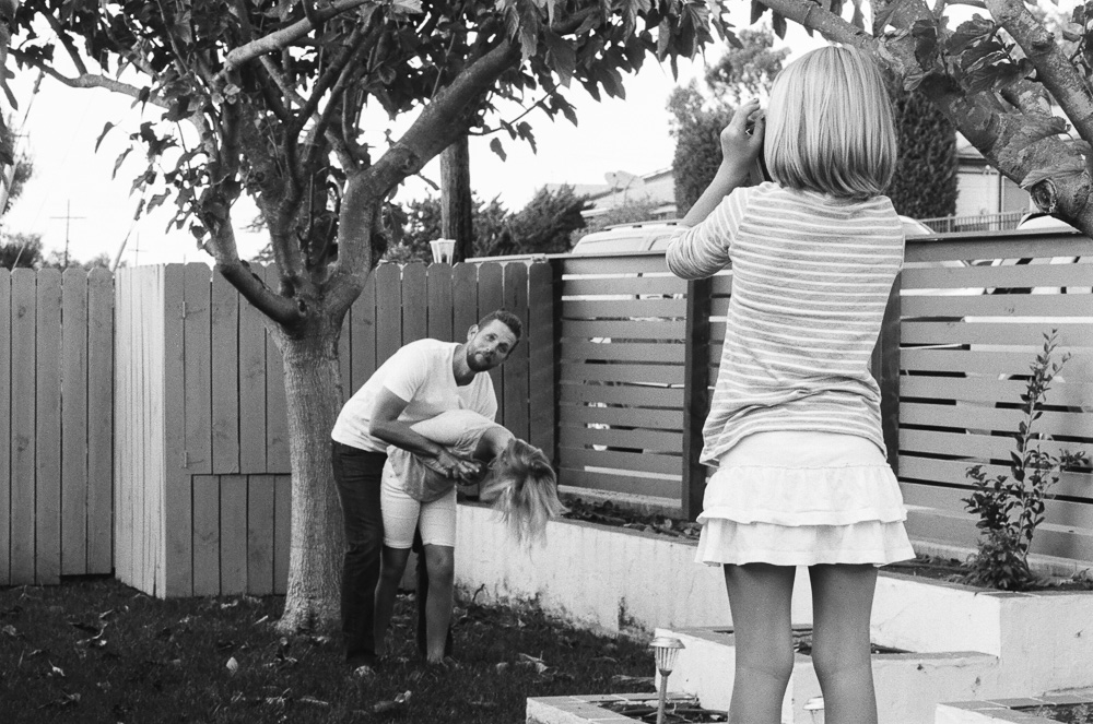 Dad (Jeff), and daughter (Kate) wrestle in the front yard while Alex takes a photo. ©William Bay Photographic Arts.